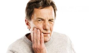 Older man holding his jaw in discomfort, indicating tooth pain or gum disease symptoms, relevant to discussions on periodontal health and treatment options.